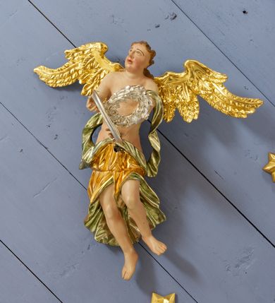 Zdjęcie nr 10: Drewniany, polichromowany na niebiesko strop, na planie ośmioboku, ujęty profilowaną ramą. W jego centrum grupa Koronacji Marii w glorii promienistej. W środku grupy figura Matki Boskiej na tle opaski dekorowanej kwiatami. Maria ukazana frontalnie, w kontrapoście, z rękami złożonymi w geście modlitwy. Twarz ma pociągłą, szczupłą, o młodzieńczych rysach, okoloną długimi włosami, upiętymi z tyłu głowy. Ubrana jest w srebrzoną suknię oraz złocony płaszcz narzucony na ramiona i zawinięty na lewej nodze, na głowie ma koronę zamkniętą. Marię flankują dwie banderole z napisem: „FIAT”. Po jej prawej znacznie większa figura Chrystusa, ukazanego frontalnie, w pozycji siedzącej, z głową skierowaną do wewnątrz; jego lewa ręka spoczywa na piersi, prawa jest ugięta i uniesiona w geście wskazującym. Twarz ma pociągłą, szczupłą, okoloną brodą skręconą w dwa pukle, oraz kręconymi włosami. Chrystus przewiązany jest w partii bioder złoconym płaszczem otaczającym postać i odsłaniającym lewą nogę. Jego ciało w odsłoniętych partiach, ma delikatnie zarysowaną muskulaturę, z zaznaczonymi śladami męki. Po lewej stronie Marii znacznie większa figura Boga Ojca, ukazanego frontalnie, w pozycji siedzącej. Lewą ręką przytrzymuje jabłko królewskie, w dłoni dzierży berło, prawą wyciąga w geście błogosławieństwa. Twarz ma pociągłą, o starczych rysach, okoloną długą, kręconą brodą opadającą na pierś oraz krótkimi włosami. Ubrany jest w obficie drapowaną srebrzoną tunikę, przepasaną w talii oraz złocony płaszcz z dekoracyjną, kameryzowaną lamówką, zapięty na piersi i opadający na boki, z zawiniętym fragmentem tkaniny na lewej nodze. Nad postaciami nadlatująca gołębica Ducha Świętego w glorii promienistej z banderolą z napisem: „FIAT”. Grupa na tle trzystrefowej glorii promienistej dekorowanej gwiazdami i uskrzydlonymi główkami anielskimi. Glorię z grupą Koronacji otacza dwunastu aniołów, ułożonych naprzemiennie w cztery pary muzykujących postaci (ze skrzypcami, wiolonczelą, gitarą, trąbką, harfą) z czterema aniołami podtrzymującymi tace z symbolicznymi przedmiotami (różaniec, wieniec laurowy, chleb (?), dyscyplina). Strop dekorowany jest w całości gwiazdami i uskrzydlonymi główkami anielskimi. Figury w partiach ciała polichromowane są naturalistycznie, ich szaty są złocone, srebrzone i laserowane; atrybuty są srebrzone. 

