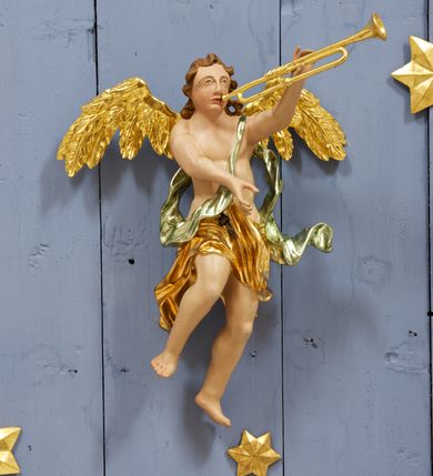 Zdjęcie nr 12: Drewniany, polichromowany na niebiesko strop, na planie ośmioboku, ujęty profilowaną ramą. W jego centrum grupa Koronacji Marii w glorii promienistej. W środku grupy figura Matki Boskiej na tle opaski dekorowanej kwiatami. Maria ukazana frontalnie, w kontrapoście, z rękami złożonymi w geście modlitwy. Twarz ma pociągłą, szczupłą, o młodzieńczych rysach, okoloną długimi włosami, upiętymi z tyłu głowy. Ubrana jest w srebrzoną suknię oraz złocony płaszcz narzucony na ramiona i zawinięty na lewej nodze, na głowie ma koronę zamkniętą. Marię flankują dwie banderole z napisem: „FIAT”. Po jej prawej znacznie większa figura Chrystusa, ukazanego frontalnie, w pozycji siedzącej, z głową skierowaną do wewnątrz; jego lewa ręka spoczywa na piersi, prawa jest ugięta i uniesiona w geście wskazującym. Twarz ma pociągłą, szczupłą, okoloną brodą skręconą w dwa pukle, oraz kręconymi włosami. Chrystus przewiązany jest w partii bioder złoconym płaszczem otaczającym postać i odsłaniającym lewą nogę. Jego ciało w odsłoniętych partiach, ma delikatnie zarysowaną muskulaturę, z zaznaczonymi śladami męki. Po lewej stronie Marii znacznie większa figura Boga Ojca, ukazanego frontalnie, w pozycji siedzącej. Lewą ręką przytrzymuje jabłko królewskie, w dłoni dzierży berło, prawą wyciąga w geście błogosławieństwa. Twarz ma pociągłą, o starczych rysach, okoloną długą, kręconą brodą opadającą na pierś oraz krótkimi włosami. Ubrany jest w obficie drapowaną srebrzoną tunikę, przepasaną w talii oraz złocony płaszcz z dekoracyjną, kameryzowaną lamówką, zapięty na piersi i opadający na boki, z zawiniętym fragmentem tkaniny na lewej nodze. Nad postaciami nadlatująca gołębica Ducha Świętego w glorii promienistej z banderolą z napisem: „FIAT”. Grupa na tle trzystrefowej glorii promienistej dekorowanej gwiazdami i uskrzydlonymi główkami anielskimi. Glorię z grupą Koronacji otacza dwunastu aniołów, ułożonych naprzemiennie w cztery pary muzykujących postaci (ze skrzypcami, wiolonczelą, gitarą, trąbką, harfą) z czterema aniołami podtrzymującymi tace z symbolicznymi przedmiotami (różaniec, wieniec laurowy, chleb (?), dyscyplina). Strop dekorowany jest w całości gwiazdami i uskrzydlonymi główkami anielskimi. Figury w partiach ciała polichromowane są naturalistycznie, ich szaty są złocone, srebrzone i laserowane; atrybuty są srebrzone. 

