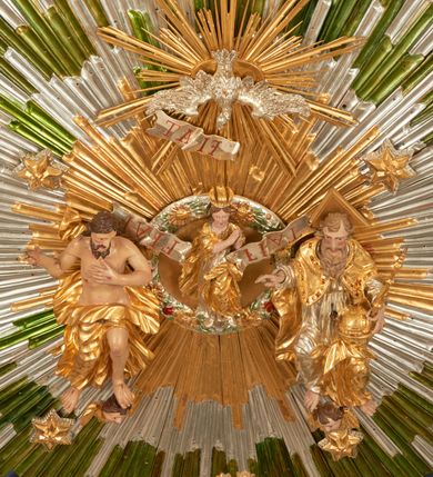 Zdjęcie nr 1: Drewniany, polichromowany na niebiesko strop, na planie ośmioboku, ujęty profilowaną ramą. W jego centrum grupa Koronacji Marii w glorii promienistej. W środku grupy figura Matki Boskiej na tle opaski dekorowanej kwiatami. Maria ukazana frontalnie, w kontrapoście, z rękami złożonymi w geście modlitwy. Twarz ma pociągłą, szczupłą, o młodzieńczych rysach, okoloną długimi włosami, upiętymi z tyłu głowy. Ubrana jest w srebrzoną suknię oraz złocony płaszcz narzucony na ramiona i zawinięty na lewej nodze, na głowie ma koronę zamkniętą. Marię flankują dwie banderole z napisem: „FIAT”. Po jej prawej znacznie większa figura Chrystusa, ukazanego frontalnie, w pozycji siedzącej, z głową skierowaną do wewnątrz; jego lewa ręka spoczywa na piersi, prawa jest ugięta i uniesiona w geście wskazującym. Twarz ma pociągłą, szczupłą, okoloną brodą skręconą w dwa pukle, oraz kręconymi włosami. Chrystus przewiązany jest w partii bioder złoconym płaszczem otaczającym postać i odsłaniającym lewą nogę. Jego ciało w odsłoniętych partiach, ma delikatnie zarysowaną muskulaturę, z zaznaczonymi śladami męki. Po lewej stronie Marii znacznie większa figura Boga Ojca, ukazanego frontalnie, w pozycji siedzącej. Lewą ręką przytrzymuje jabłko królewskie, w dłoni dzierży berło, prawą wyciąga w geście błogosławieństwa. Twarz ma pociągłą, o starczych rysach, okoloną długą, kręconą brodą opadającą na pierś oraz krótkimi włosami. Ubrany jest w obficie drapowaną srebrzoną tunikę, przepasaną w talii oraz złocony płaszcz z dekoracyjną, kameryzowaną lamówką, zapięty na piersi i opadający na boki, z zawiniętym fragmentem tkaniny na lewej nodze. Nad postaciami nadlatująca gołębica Ducha Świętego w glorii promienistej z banderolą z napisem: „FIAT”. Grupa na tle trzystrefowej glorii promienistej dekorowanej gwiazdami i uskrzydlonymi główkami anielskimi. Glorię z grupą Koronacji otacza dwunastu aniołów, ułożonych naprzemiennie w cztery pary muzykujących postaci (ze skrzypcami, wiolonczelą, gitarą, trąbką, harfą) z czterema aniołami podtrzymującymi tace z symbolicznymi przedmiotami (różaniec, wieniec laurowy, chleb (?), dyscyplina). Strop dekorowany jest w całości gwiazdami i uskrzydlonymi główkami anielskimi. Figury w partiach ciała polichromowane są naturalistycznie, ich szaty są złocone, srebrzone i laserowane; atrybuty są srebrzone. 

