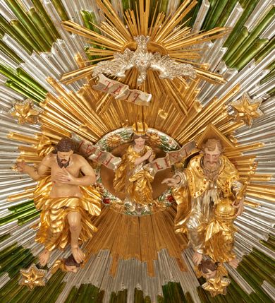 Zdjęcie nr 3: Drewniany, polichromowany na niebiesko strop, na planie ośmioboku, ujęty profilowaną ramą. W jego centrum grupa Koronacji Marii w glorii promienistej. W środku grupy figura Matki Boskiej na tle opaski dekorowanej kwiatami. Maria ukazana frontalnie, w kontrapoście, z rękami złożonymi w geście modlitwy. Twarz ma pociągłą, szczupłą, o młodzieńczych rysach, okoloną długimi włosami, upiętymi z tyłu głowy. Ubrana jest w srebrzoną suknię oraz złocony płaszcz narzucony na ramiona i zawinięty na lewej nodze, na głowie ma koronę zamkniętą. Marię flankują dwie banderole z napisem: „FIAT”. Po jej prawej znacznie większa figura Chrystusa, ukazanego frontalnie, w pozycji siedzącej, z głową skierowaną do wewnątrz; jego lewa ręka spoczywa na piersi, prawa jest ugięta i uniesiona w geście wskazującym. Twarz ma pociągłą, szczupłą, okoloną brodą skręconą w dwa pukle, oraz kręconymi włosami. Chrystus przewiązany jest w partii bioder złoconym płaszczem otaczającym postać i odsłaniającym lewą nogę. Jego ciało w odsłoniętych partiach, ma delikatnie zarysowaną muskulaturę, z zaznaczonymi śladami męki. Po lewej stronie Marii znacznie większa figura Boga Ojca, ukazanego frontalnie, w pozycji siedzącej. Lewą ręką przytrzymuje jabłko królewskie, w dłoni dzierży berło, prawą wyciąga w geście błogosławieństwa. Twarz ma pociągłą, o starczych rysach, okoloną długą, kręconą brodą opadającą na pierś oraz krótkimi włosami. Ubrany jest w obficie drapowaną srebrzoną tunikę, przepasaną w talii oraz złocony płaszcz z dekoracyjną, kameryzowaną lamówką, zapięty na piersi i opadający na boki, z zawiniętym fragmentem tkaniny na lewej nodze. Nad postaciami nadlatująca gołębica Ducha Świętego w glorii promienistej z banderolą z napisem: „FIAT”. Grupa na tle trzystrefowej glorii promienistej dekorowanej gwiazdami i uskrzydlonymi główkami anielskimi. Glorię z grupą Koronacji otacza dwunastu aniołów, ułożonych naprzemiennie w cztery pary muzykujących postaci (ze skrzypcami, wiolonczelą, gitarą, trąbką, harfą) z czterema aniołami podtrzymującymi tace z symbolicznymi przedmiotami (różaniec, wieniec laurowy, chleb (?), dyscyplina). Strop dekorowany jest w całości gwiazdami i uskrzydlonymi główkami anielskimi. Figury w partiach ciała polichromowane są naturalistycznie, ich szaty są złocone, srebrzone i laserowane; atrybuty są srebrzone. 

