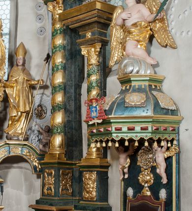 Zdjęcie nr 10: Nastawa ołtarzowa architektoniczna, trójosiowa z bramkami, dwukondygnacyjna, na dwustrefowym cokole. Ołtarz kamienny, prostopadłościenny, w drewnianej obudowie. Antepedium w formie wydłużonego, leżącego prostokąta, w polu obraz Ostatniej Wieczerzy. Mensa drewniana. Osie nastawy wydzielone parą półfilarów ujętych dwiema parami kolumn o kapitelach kompozytowych i skręconych trzonach. Dźwigają one pełne belkowanie silnie wyłamane na osi filarów, z mocno wysuniętym gzymsem, na skraju belkowania przerwany półkolisty przyczółek zwrócony na zewnątrz, na nim cokoły z figurami św. Władysława i św. Stefana. Na tle filarów ustawione figury św. Augustyna i św. Wojciecha, na bramkach rzeźby św. Marcina i św. Jana Jałmużnika. W polu głównym głęboka nisza w formie kwadratu zamkniętego łukiem falistym nadwieszonym, wewnątrz rzeźbiarska scena „Zabójstwa św. Stanisława”. Druga kondygnacja ujęta półfilarami, na tle których znajdują się anioły-kariatydy siedzące na cokołach z wolutami, podtrzymujące imposty. W polu prześwit w formie stojącego prostokąta z wpisanym krzyżem w kształcie litery „X”, przed którym znajduje się figura św. Andrzeja. Całość zwieńczona półpostacią Boga Ojca wśród obłoków i uskrzydlonych główek anielskich w glorii promienistej. Struktura obficie dekorowana ornamentem roślinnym, w partii pierwszej i drugiej kondygnacji uszy utworzone z akantu i wstęgi. Ołtarz flankują dodatkowo dwie pary wolnostojących półfilarów z półkolumnami o skręconych trzonach przed nimi, stojących na dwustrefowych cokołach, dźwigających imposty z figurami. Na zewnętrznej, niższej parze znajdują się figury św. Jana Ewangelisty i św. Jana Chrzciciela, na wewnętrznej, wyższej parze – św. Piotra i św. Pawła. Struktura polichromowana w sposób naśladujący marmoryzację w kolorze niebiesko-szarym, z zielonymi profilami oraz złoconymi kolumnami, profilami i ornamentyką.


