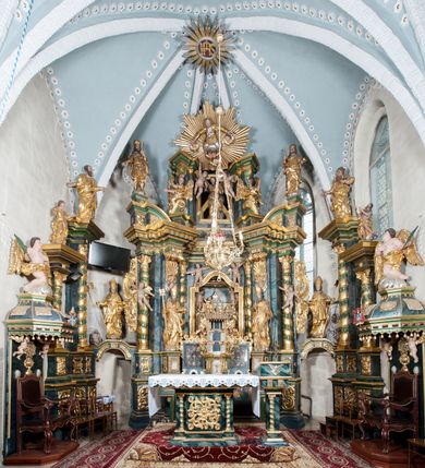 Zdjęcie nr 3: Nastawa ołtarzowa architektoniczna, trójosiowa z bramkami, dwukondygnacyjna, na dwustrefowym cokole. Ołtarz kamienny, prostopadłościenny, w drewnianej obudowie. Antepedium w formie wydłużonego, leżącego prostokąta, w polu obraz Ostatniej Wieczerzy. Mensa drewniana. Osie nastawy wydzielone parą półfilarów ujętych dwiema parami kolumn o kapitelach kompozytowych i skręconych trzonach. Dźwigają one pełne belkowanie silnie wyłamane na osi filarów, z mocno wysuniętym gzymsem, na skraju belkowania przerwany półkolisty przyczółek zwrócony na zewnątrz, na nim cokoły z figurami św. Władysława i św. Stefana. Na tle filarów ustawione figury św. Augustyna i św. Wojciecha, na bramkach rzeźby św. Marcina i św. Jana Jałmużnika. W polu głównym głęboka nisza w formie kwadratu zamkniętego łukiem falistym nadwieszonym, wewnątrz rzeźbiarska scena „Zabójstwa św. Stanisława”. Druga kondygnacja ujęta półfilarami, na tle których znajdują się anioły-kariatydy siedzące na cokołach z wolutami, podtrzymujące imposty. W polu prześwit w formie stojącego prostokąta z wpisanym krzyżem w kształcie litery „X”, przed którym znajduje się figura św. Andrzeja. Całość zwieńczona półpostacią Boga Ojca wśród obłoków i uskrzydlonych główek anielskich w glorii promienistej. Struktura obficie dekorowana ornamentem roślinnym, w partii pierwszej i drugiej kondygnacji uszy utworzone z akantu i wstęgi. Ołtarz flankują dodatkowo dwie pary wolnostojących półfilarów z półkolumnami o skręconych trzonach przed nimi, stojących na dwustrefowych cokołach, dźwigających imposty z figurami. Na zewnętrznej, niższej parze znajdują się figury św. Jana Ewangelisty i św. Jana Chrzciciela, na wewnętrznej, wyższej parze – św. Piotra i św. Pawła. Struktura polichromowana w sposób naśladujący marmoryzację w kolorze niebiesko-szarym, z zielonymi profilami oraz złoconymi kolumnami, profilami i ornamentyką.


