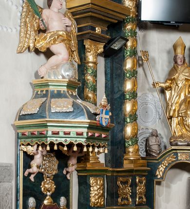 Zdjęcie nr 11: Nastawa ołtarzowa architektoniczna, trójosiowa z bramkami, dwukondygnacyjna, na dwustrefowym cokole. Ołtarz kamienny, prostopadłościenny, w drewnianej obudowie. Antepedium w formie wydłużonego, leżącego prostokąta, w polu obraz Ostatniej Wieczerzy. Mensa drewniana. Osie nastawy wydzielone parą półfilarów ujętych dwiema parami kolumn o kapitelach kompozytowych i skręconych trzonach. Dźwigają one pełne belkowanie silnie wyłamane na osi filarów, z mocno wysuniętym gzymsem, na skraju belkowania przerwany półkolisty przyczółek zwrócony na zewnątrz, na nim cokoły z figurami św. Władysława i św. Stefana. Na tle filarów ustawione figury św. Augustyna i św. Wojciecha, na bramkach rzeźby św. Marcina i św. Jana Jałmużnika. W polu głównym głęboka nisza w formie kwadratu zamkniętego łukiem falistym nadwieszonym, wewnątrz rzeźbiarska scena „Zabójstwa św. Stanisława”. Druga kondygnacja ujęta półfilarami, na tle których znajdują się anioły-kariatydy siedzące na cokołach z wolutami, podtrzymujące imposty. W polu prześwit w formie stojącego prostokąta z wpisanym krzyżem w kształcie litery „X”, przed którym znajduje się figura św. Andrzeja. Całość zwieńczona półpostacią Boga Ojca wśród obłoków i uskrzydlonych główek anielskich w glorii promienistej. Struktura obficie dekorowana ornamentem roślinnym, w partii pierwszej i drugiej kondygnacji uszy utworzone z akantu i wstęgi. Ołtarz flankują dodatkowo dwie pary wolnostojących półfilarów z półkolumnami o skręconych trzonach przed nimi, stojących na dwustrefowych cokołach, dźwigających imposty z figurami. Na zewnętrznej, niższej parze znajdują się figury św. Jana Ewangelisty i św. Jana Chrzciciela, na wewnętrznej, wyższej parze – św. Piotra i św. Pawła. Struktura polichromowana w sposób naśladujący marmoryzację w kolorze niebiesko-szarym, z zielonymi profilami oraz złoconymi kolumnami, profilami i ornamentyką.


