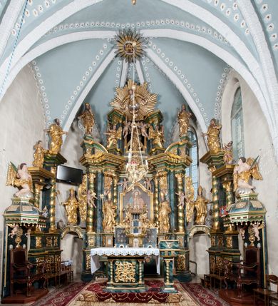 Zdjęcie nr 4: Nastawa ołtarzowa architektoniczna, trójosiowa z bramkami, dwukondygnacyjna, na dwustrefowym cokole. Ołtarz kamienny, prostopadłościenny, w drewnianej obudowie. Antepedium w formie wydłużonego, leżącego prostokąta, w polu obraz Ostatniej Wieczerzy. Mensa drewniana. Osie nastawy wydzielone parą półfilarów ujętych dwiema parami kolumn o kapitelach kompozytowych i skręconych trzonach. Dźwigają one pełne belkowanie silnie wyłamane na osi filarów, z mocno wysuniętym gzymsem, na skraju belkowania przerwany półkolisty przyczółek zwrócony na zewnątrz, na nim cokoły z figurami św. Władysława i św. Stefana. Na tle filarów ustawione figury św. Augustyna i św. Wojciecha, na bramkach rzeźby św. Marcina i św. Jana Jałmużnika. W polu głównym głęboka nisza w formie kwadratu zamkniętego łukiem falistym nadwieszonym, wewnątrz rzeźbiarska scena „Zabójstwa św. Stanisława”. Druga kondygnacja ujęta półfilarami, na tle których znajdują się anioły-kariatydy siedzące na cokołach z wolutami, podtrzymujące imposty. W polu prześwit w formie stojącego prostokąta z wpisanym krzyżem w kształcie litery „X”, przed którym znajduje się figura św. Andrzeja. Całość zwieńczona półpostacią Boga Ojca wśród obłoków i uskrzydlonych główek anielskich w glorii promienistej. Struktura obficie dekorowana ornamentem roślinnym, w partii pierwszej i drugiej kondygnacji uszy utworzone z akantu i wstęgi. Ołtarz flankują dodatkowo dwie pary wolnostojących półfilarów z półkolumnami o skręconych trzonach przed nimi, stojących na dwustrefowych cokołach, dźwigających imposty z figurami. Na zewnętrznej, niższej parze znajdują się figury św. Jana Ewangelisty i św. Jana Chrzciciela, na wewnętrznej, wyższej parze – św. Piotra i św. Pawła. Struktura polichromowana w sposób naśladujący marmoryzację w kolorze niebiesko-szarym, z zielonymi profilami oraz złoconymi kolumnami, profilami i ornamentyką.


