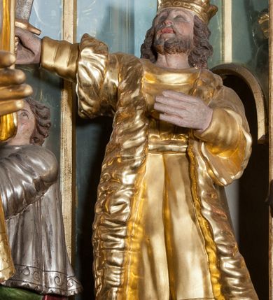 Zdjęcie nr 15: Nastawa ołtarzowa architektoniczna, trójosiowa z bramkami, dwukondygnacyjna, na dwustrefowym cokole. Ołtarz kamienny, prostopadłościenny, w drewnianej obudowie. Antepedium w formie wydłużonego, leżącego prostokąta, w polu obraz Ostatniej Wieczerzy. Mensa drewniana. Osie nastawy wydzielone parą półfilarów ujętych dwiema parami kolumn o kapitelach kompozytowych i skręconych trzonach. Dźwigają one pełne belkowanie silnie wyłamane na osi filarów, z mocno wysuniętym gzymsem, na skraju belkowania przerwany półkolisty przyczółek zwrócony na zewnątrz, na nim cokoły z figurami św. Władysława i św. Stefana. Na tle filarów ustawione figury św. Augustyna i św. Wojciecha, na bramkach rzeźby św. Marcina i św. Jana Jałmużnika. W polu głównym głęboka nisza w formie kwadratu zamkniętego łukiem falistym nadwieszonym, wewnątrz rzeźbiarska scena „Zabójstwa św. Stanisława”. Druga kondygnacja ujęta półfilarami, na tle których znajdują się anioły-kariatydy siedzące na cokołach z wolutami, podtrzymujące imposty. W polu prześwit w formie stojącego prostokąta z wpisanym krzyżem w kształcie litery „X”, przed którym znajduje się figura św. Andrzeja. Całość zwieńczona półpostacią Boga Ojca wśród obłoków i uskrzydlonych główek anielskich w glorii promienistej. Struktura obficie dekorowana ornamentem roślinnym, w partii pierwszej i drugiej kondygnacji uszy utworzone z akantu i wstęgi. Ołtarz flankują dodatkowo dwie pary wolnostojących półfilarów z półkolumnami o skręconych trzonach przed nimi, stojących na dwustrefowych cokołach, dźwigających imposty z figurami. Na zewnętrznej, niższej parze znajdują się figury św. Jana Ewangelisty i św. Jana Chrzciciela, na wewnętrznej, wyższej parze – św. Piotra i św. Pawła. Struktura polichromowana w sposób naśladujący marmoryzację w kolorze niebiesko-szarym, z zielonymi profilami oraz złoconymi kolumnami, profilami i ornamentyką.


