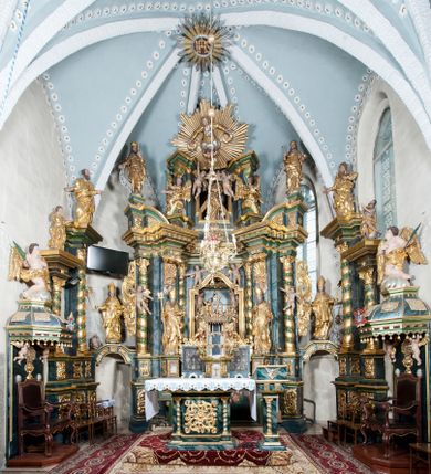 Zdjęcie nr 1: Nastawa ołtarzowa architektoniczna, trójosiowa z bramkami, dwukondygnacyjna, na dwustrefowym cokole. Ołtarz kamienny, prostopadłościenny, w drewnianej obudowie. Antepedium w formie wydłużonego, leżącego prostokąta, w polu obraz Ostatniej Wieczerzy. Mensa drewniana. Osie nastawy wydzielone parą półfilarów ujętych dwiema parami kolumn o kapitelach kompozytowych i skręconych trzonach. Dźwigają one pełne belkowanie silnie wyłamane na osi filarów, z mocno wysuniętym gzymsem, na skraju belkowania przerwany półkolisty przyczółek zwrócony na zewnątrz, na nim cokoły z figurami św. Władysława i św. Stefana. Na tle filarów ustawione figury św. Augustyna i św. Wojciecha, na bramkach rzeźby św. Marcina i św. Jana Jałmużnika. W polu głównym głęboka nisza w formie kwadratu zamkniętego łukiem falistym nadwieszonym, wewnątrz rzeźbiarska scena „Zabójstwa św. Stanisława”. Druga kondygnacja ujęta półfilarami, na tle których znajdują się anioły-kariatydy siedzące na cokołach z wolutami, podtrzymujące imposty. W polu prześwit w formie stojącego prostokąta z wpisanym krzyżem w kształcie litery „X”, przed którym znajduje się figura św. Andrzeja. Całość zwieńczona półpostacią Boga Ojca wśród obłoków i uskrzydlonych główek anielskich w glorii promienistej. Struktura obficie dekorowana ornamentem roślinnym, w partii pierwszej i drugiej kondygnacji uszy utworzone z akantu i wstęgi. Ołtarz flankują dodatkowo dwie pary wolnostojących półfilarów z półkolumnami o skręconych trzonach przed nimi, stojących na dwustrefowych cokołach, dźwigających imposty z figurami. Na zewnętrznej, niższej parze znajdują się figury św. Jana Ewangelisty i św. Jana Chrzciciela, na wewnętrznej, wyższej parze – św. Piotra i św. Pawła. Struktura polichromowana w sposób naśladujący marmoryzację w kolorze niebiesko-szarym, z zielonymi profilami oraz złoconymi kolumnami, profilami i ornamentyką.


