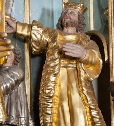 Zdjęcie nr 4: W głębokiej wnęce wyłożonej z trzech stron lustrami znajduje się grupa figuralna ze sceną zabójstwa św. Stanisława. Przed złoconym ołtarzem ustawionym na dwustopniowej podstawie figura św. Stanisława ukazana z lewego profilu w momencie podniesienia, z hostią w dłoniach. Święty jest ubrany w albę i ornat, z manipularzem na przedramieniu. U jego prawego boku, na najniższym stopniu klęczy ministrant ubrany w  komżę z uniesioną ręką, w której trzyma dzwonek. Za ich plecami figura króla Bolesława Szczodrego ustawiona na dwustopniowym postumencie, zwrócona w trzech czwartych w lewo, z uniesionym mieczem trzymanym w prawej ręce. Król jest ubrany w tunikę przewiązaną w pasie, płaszcz królewski i wysokie buty, na głowie ma koronę otwartą. Polichromia naturalistyczna w partiach ciała, szaty złocone i srebrzone.