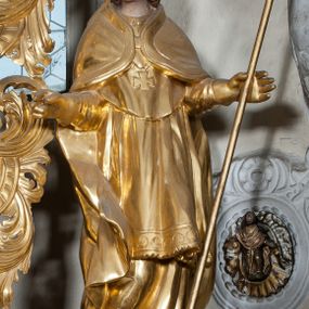 Zdjęcie nr 1: Figura ścięta z tyłu, ustawiona jest na obłoku, ukazana frontalnie z głową skierowaną w prawo, w kontrapoście, o esowato wygiętej sylwetce, z rękami rozłożonymi na boki, w lewej trzyma pastorał. Twarz ma owalną, pełną, o oczach wzniesionych w górę, ustach lekko rozchylonych, okoloną falowanymi, sięgającymi ramion włosami. Święty ubrany jest w strój biskupi: albę, rokietę i mucet, na szyi ma zawieszony pektorał, na dłoniach rękawiczki, a na głowie infułę. Ramiona okrywa kapa spięta na piersi, z rozwianą na prawy bok fałdą. Po lewej stronie świętego niewielka, klęcząca postać kalekiego mężczyzny, wspierającego się lewą ręką na kulach, z wyciągniętą ku górze prawą ręką. Polichromia naturalistyczna w partiach ciała, szaty i atrybuty pozłacane.