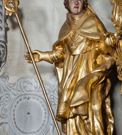 Zdjęcie nr 1: Figura ścięta z tyłu, stojąca na obłoku, ukazana frontalnie z głową zwróconą w lewą stronę, sylwetka esowato wygięta, ręce rozchylone na boki, w prawej trzyma pastorał. Twarz świętego owalna, pełna, oczy skierowane ku górze, usta lekko rozchylone, okolona krótkimi, falowanymi włosami, sięgającymi ramion. Marcin jest ubrany w szaty biskupie: albę, rokietę i mucet, na głowie ma infułę, na piersi zawieszony pektorał, na dłoniach rękawiczki. Ramiona okrywa kapa spięta na piersi, z rozwianą fałdą przy jego lewym boku. Obok świętego, po jego prawej, półpostać zwrócona w trzech czwartych w prawo, z rękoma złożonymi w geście modlitwy. Szaty postaci złocone, karnacja ciała w odcieniu jasnokremowym. 