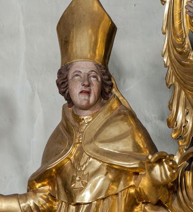 Zdjęcie nr 3: Figura ścięta z tyłu, stojąca na obłoku, ukazana frontalnie z głową zwróconą w lewą stronę, sylwetka esowato wygięta, ręce rozchylone na boki, w prawej trzyma pastorał. Twarz świętego owalna, pełna, oczy skierowane ku górze, usta lekko rozchylone, okolona krótkimi, falowanymi włosami, sięgającymi ramion. Marcin jest ubrany w szaty biskupie: albę, rokietę i mucet, na głowie ma infułę, na piersi zawieszony pektorał, na dłoniach rękawiczki. Ramiona okrywa kapa spięta na piersi, z rozwianą fałdą przy jego lewym boku. Obok świętego, po jego prawej, półpostać zwrócona w trzech czwartych w prawo, z rękoma złożonymi w geście modlitwy. Szaty postaci złocone, karnacja ciała w odcieniu jasnokremowym. 