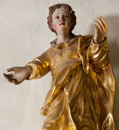 Zdjęcie nr 1: Rzeźba drążona, ustawiona jest frontalnie, w kontrapoście, z lewą ręką wyciągniętą do przodu, prawą w bok. Święty ma pełną twarz, o młodzieńczych rysach, dużych oczach, zadartym nosie, pełnych, rozchylonych ustach, okoloną krótkimi, kręconymi włosami, opadającymi na tył głowy i kark. Ubrany jest w przylegającą do ciała tunikę z kołnierzykiem oraz płaszcz przerzucony przez lewe ramię i opasujący korpus. Polichromia naturalistyczna w odsłoniętych partiach ciała, szaty pozłocone.
