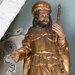 Zdjęcie nr 1: Figura jest drążona z tyłu, ustawiona na rzeźbionym obłoku, zwrócona frontalnie. Święty w lewej ręce wysuniętej przed siebie trzyma berło, w prawej wyciągniętej w bok banderolę z napisem „SPES MEA IN DEO”. Twarz ma kwadratową, o dużych oczach, niewielkim nosie i pełnych ustach, okoloną krótką, gęstą brodą oraz kręconymi włosami sięgającymi ramion. Ubrany jest w tunikę sięgającą ramion, zbroję torsową, spodnie i wysokie buty, na ramionach ma płaszcz z kołnierzem, na głowie koronę zamkniętą. Polichromia naturalistyczna w odsłoniętych partiach ciała, strój i atrybuty pozłocone.