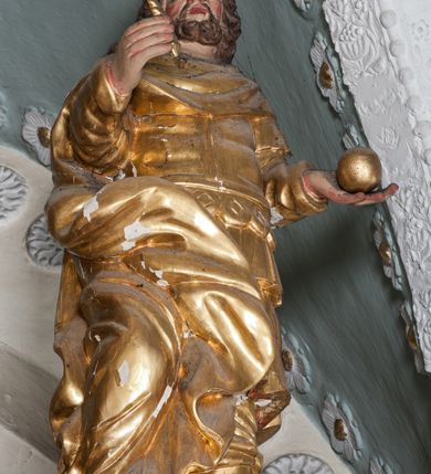 Zdjęcie nr 3: Figura ustawiona jest na rzeźbionym obłoku, zwrócona frontalnie, w kontrapoście, w lewej, wyciągniętej w bok ręce trzyma kulę (jabłko królewskie?), w prawej, wysuniętej w przód – berło. Twarz świętego kwadratowa, z oczami skierowanymi w górę, małym nosem i rozchylonymi ustami, okolona krótką brodą oraz sięgającymi ramion, kręconymi włosami. Stefan jest ubrany w suknię sięgającą kolan, zbroję torsową oraz płaszcz zawinięty na prawej nodze, spodnie i wysokie buty, na głowie ma koronę zamkniętą. Polichromia naturalistyczna w odsłoniętych partiach ciała, strój i atrybuty pozłacane.