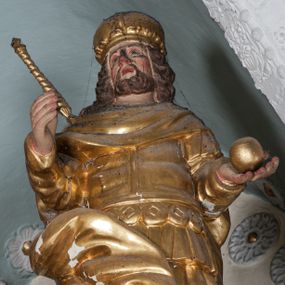 Zdjęcie nr 1: Figura ustawiona jest na rzeźbionym obłoku, zwrócona frontalnie, w kontrapoście, w lewej, wyciągniętej w bok ręce trzyma kulę (jabłko królewskie?), w prawej, wysuniętej w przód – berło. Twarz świętego kwadratowa, z oczami skierowanymi w górę, małym nosem i rozchylonymi ustami, okolona krótką brodą oraz sięgającymi ramion, kręconymi włosami. Stefan jest ubrany w suknię sięgającą kolan, zbroję torsową oraz płaszcz zawinięty na prawej nodze, spodnie i wysokie buty, na głowie ma koronę zamkniętą. Polichromia naturalistyczna w odsłoniętych partiach ciała, strój i atrybuty pozłacane.
