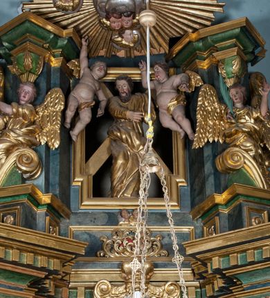 Zdjęcie nr 3: Rzeźba drążona, ustawiona na tle krzyża w formie litery „X” ujętego w profilowaną ramę. Figura zwrócona jest frontalnie, w kontrapoście, lewą ręką ujmuje ramię krzyża, prawą wyciąga przed siebie. Twarz ma pociągłą, nos prosty, oczy skierowane w dół, usta rozchylone, okoloną brodą skręconą w pukle oraz krótkimi włosami. Postać jest ubrana w suknię ściśle przylegającą do ciała, przepasaną w talii oraz płaszcz zarzucony na lewe ramię oraz opadający na kolana w postaci skręconej tkaniny. Polichromia naturalistyczna w odsłoniętych partiach ciała, strój i krzyż pozłocone. 