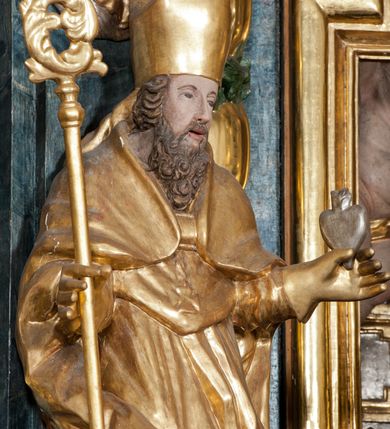 Zdjęcie nr 3: Rzeźba ścięta z tyłu, ustawiona jest na obłoku, zwrócona frontalnie, o esowato wygiętej sylwetce, z rękoma rozłożonymi na boki. Święty w lewej dłoni trzyma gorejące serce, w prawej pastorał. Twarz ma pociągłą o prostym nosie, głęboko rzeźbionej górnej powiece oraz szerokich, rozchylonych ustach, okoloną gęstą brodą, silnie kręconą oraz krótkimi włosami. Ubrany jest w albę, komżę, mucet i kapę, na piersi ma krzyż pektoralny, na głowie infułę, na dłoniach zaś rękawiczki. Polichromia naturalistyczna w odsłoniętych partiach ciała, strój i pastorał pozłocone, serce posrebrzone.
