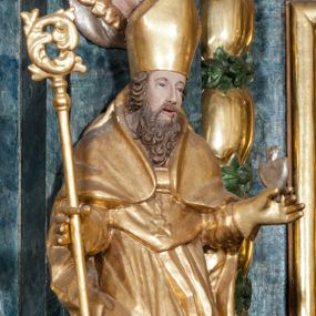 Zdjęcie nr 1: Rzeźba ścięta z tyłu, ustawiona jest na obłoku, zwrócona frontalnie, o esowato wygiętej sylwetce, z rękoma rozłożonymi na boki. Święty w lewej dłoni trzyma gorejące serce, w prawej pastorał. Twarz ma pociągłą o prostym nosie, głęboko rzeźbionej górnej powiece oraz szerokich, rozchylonych ustach, okoloną gęstą brodą, silnie kręconą oraz krótkimi włosami. Ubrany jest w albę, komżę, mucet i kapę, na piersi ma krzyż pektoralny, na głowie infułę, na dłoniach zaś rękawiczki. Polichromia naturalistyczna w odsłoniętych partiach ciała, strój i pastorał pozłocone, serce posrebrzone.