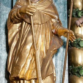 Zdjęcie nr 1: Rzeźba ścięta z tyłu, zwrócona jest w trzech czwartych w prawo, w kontrapoście, o esowato wygiętej sylwetce. Święty w lewej wyciągniętej w bok ręce trzyma pastorał, w prawej wiosło. Twarz ma pociągłą o prostym nosie, głęboko rzeźbionej górnej powiece, rozchylonych, pełnych ustach, okoloną brodą skręconą w dwa pukle oraz krótkimi włosami. Ubrany jest w albę, rokietę, mucet, kapę oraz paliusz, na głowie ma infułę, na dłoniach rękawiczki. Rzeźba polichromowana naturalistycznie w odsłoniętych partiach ciała, strój i atrybuty pozłocone.