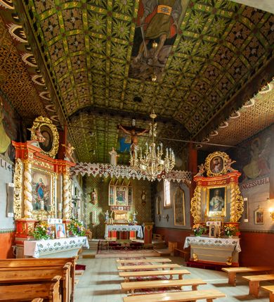 Zdjęcie nr 11: Polichromia pokrywa praktycznie całe wnętrze kościoła wraz z przedsionkiem. Przy wejściu, na stropie pod wieżą znajduje się polichromia patronowa. Jest wielobrawna, z motywami architektonicznymi, geometrycznymi, roślinno-kwiatowymi i figuralnymi – jeleniami, parami gołąbków, orłami, smokami. Wśród nich postać jeźdźca z kopią i grupa ludzi udających się na polowanie, poniżej których napis „Odbudowę kościoła, urządzenie wnętrza i rekonstrukcję dokonano staraniem Ks(iędza) Andrzeja Braszki / w czasie od lipca 1932 do grudnia r(oku) (19)39. / Pracę rozpoczął Władysław Cichoń + Skończył Adam Stalony-Dobrzański z Eugeniuszem Pisarkiem”. W polichromii przedsionka przeważają kolory  biały, czerwony, zielony, niebieski, żółty i czarny. Ponad wejściem do nawy napis  „ZACZNIJCIE / WARGI NASZE / CHWALIĆ PANNĘ / ŚWIĘTĄ / ZACZNIJCIE OPOWIADAĆ / CZEŚĆ JEJ NIEPOJĘTĄ”  i po drugieh stronie „PRZYBĄDŹ NAM. MIŁOŚCIWA PANI / KU POMOCY / A WYBAW NAS / Z RĄK POTĘŻNYCH / NIEPRZYJACIÓŁ MOCY”. Poniżej „CHWAŁA OJCU I SYNOWI JEGO PRZEDWIECZNEMU”.
W prezbiterium na ścianie i na suficie imitacja kasetonów z rozetami z przewagą koloru zielonego uzupełnionego czerwonym na ścianie i czarnym oraz bladożółtym na stropie. W centrum sufitu postać Matki Boskiej z Dzieciątkiem na lewym ramieniu, za którymi dwaj aniołowie skłaniający głowy. Maria ma poważną twarz o delikatnych rysach, ciemne oczy i wąski nos, na głowie otwartą koronę, wokół niej nimb. Jest ubrana w jasną sukienkę i intensywnie niebieski płaszcz. Dzieciątko prawą ręką błogosławi, lewą trzyma rękę Marii. Ma owalną, delikatną twarz, a na sobie jasną tunikę i zamkniętą koronę. 
W nawie, pośród takich samych kasetonów jak w prezbiterium, na sklepieniu wyobrażenie św. Michała Archanioła zabijającego szatana. Ponad nim postać anioła splatającego dłonie pod brodą. Archanioł spogląda pod stopy, w prawej ręce trzyma skierowany ostrzem w stronę potwora miecz, lewą ma opuszczoną do boku. Ma na sobie zieloną tunikę przewiązaną szerokim, góralskim pasem i czerwony płaszcz. Jasne postrzępione plamy ponad jego plecami sugerują skrzydła. Anioł powyżej jest ubrany w czerwoną sukienkę, nad nim płynnie uchodzą w górę ulistnione linie. Na ścianach nawy, pod linią stropu, rząd klęczących aniołów między kwitnącymi kwiatami. Każdy jest ubrany w zielonożółtą sukienkę i sandały, ma włosy do ramion i złoty nimb. Skrzydła z różnie ułożonych piór są wielobarwne. Anioły klęczą na linii ornamentu, ściana poniżej jest jasnoniebieska, z napisem powyżej opisanych przedstawień. 
Na skośnych fragmentach stropu imitacja drobniejszych kasetonów o falistym zarysie, wypełnionych krzyżami równoramiennymi. Wszystkie ciemnożółte, większość na czarnym tle, niektóre na tle zielonym tworzą kształt rombów. Na krawędzi motywy geometryczne, które mogą sugerować płonące serca. 
Na parapecie chóru fragmenty dawnej polichromii o motywach liściasto-wiciowych z rozwiniętymi kwiatami i motywem żołędzia. Między nimi ludzka głowa. Malowidło utrzymane w dominującym kolorze brązu, z elementami zielonymi i czerwonymi. 
