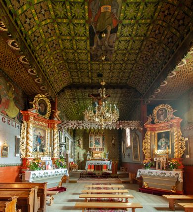 Zdjęcie nr 2: Polichromia pokrywa praktycznie całe wnętrze kościoła wraz z przedsionkiem. Przy wejściu, na stropie pod wieżą znajduje się polichromia patronowa. Jest wielobrawna, z motywami architektonicznymi, geometrycznymi, roślinno-kwiatowymi i figuralnymi – jeleniami, parami gołąbków, orłami, smokami. Wśród nich postać jeźdźca z kopią i grupa ludzi udających się na polowanie, poniżej których napis „Odbudowę kościoła, urządzenie wnętrza i rekonstrukcję dokonano staraniem Ks(iędza) Andrzeja Braszki / w czasie od lipca 1932 do grudnia r(oku) (19)39. / Pracę rozpoczął Władysław Cichoń + Skończył Adam Stalony-Dobrzański z Eugeniuszem Pisarkiem”. W polichromii przedsionka przeważają kolory  biały, czerwony, zielony, niebieski, żółty i czarny. Ponad wejściem do nawy napis  „ZACZNIJCIE / WARGI NASZE / CHWALIĆ PANNĘ / ŚWIĘTĄ / ZACZNIJCIE OPOWIADAĆ / CZEŚĆ JEJ NIEPOJĘTĄ”  i po drugieh stronie „PRZYBĄDŹ NAM. MIŁOŚCIWA PANI / KU POMOCY / A WYBAW NAS / Z RĄK POTĘŻNYCH / NIEPRZYJACIÓŁ MOCY”. Poniżej „CHWAŁA OJCU I SYNOWI JEGO PRZEDWIECZNEMU”.
W prezbiterium na ścianie i na suficie imitacja kasetonów z rozetami z przewagą koloru zielonego uzupełnionego czerwonym na ścianie i czarnym oraz bladożółtym na stropie. W centrum sufitu postać Matki Boskiej z Dzieciątkiem na lewym ramieniu, za którymi dwaj aniołowie skłaniający głowy. Maria ma poważną twarz o delikatnych rysach, ciemne oczy i wąski nos, na głowie otwartą koronę, wokół niej nimb. Jest ubrana w jasną sukienkę i intensywnie niebieski płaszcz. Dzieciątko prawą ręką błogosławi, lewą trzyma rękę Marii. Ma owalną, delikatną twarz, a na sobie jasną tunikę i zamkniętą koronę. 
W nawie, pośród takich samych kasetonów jak w prezbiterium, na sklepieniu wyobrażenie św. Michała Archanioła zabijającego szatana. Ponad nim postać anioła splatającego dłonie pod brodą. Archanioł spogląda pod stopy, w prawej ręce trzyma skierowany ostrzem w stronę potwora miecz, lewą ma opuszczoną do boku. Ma na sobie zieloną tunikę przewiązaną szerokim, góralskim pasem i czerwony płaszcz. Jasne postrzępione plamy ponad jego plecami sugerują skrzydła. Anioł powyżej jest ubrany w czerwoną sukienkę, nad nim płynnie uchodzą w górę ulistnione linie. Na ścianach nawy, pod linią stropu, rząd klęczących aniołów między kwitnącymi kwiatami. Każdy jest ubrany w zielonożółtą sukienkę i sandały, ma włosy do ramion i złoty nimb. Skrzydła z różnie ułożonych piór są wielobarwne. Anioły klęczą na linii ornamentu, ściana poniżej jest jasnoniebieska, z napisem powyżej opisanych przedstawień. 
Na skośnych fragmentach stropu imitacja drobniejszych kasetonów o falistym zarysie, wypełnionych krzyżami równoramiennymi. Wszystkie ciemnożółte, większość na czarnym tle, niektóre na tle zielonym tworzą kształt rombów. Na krawędzi motywy geometryczne, które mogą sugerować płonące serca. 
Na parapecie chóru fragmenty dawnej polichromii o motywach liściasto-wiciowych z rozwiniętymi kwiatami i motywem żołędzia. Między nimi ludzka głowa. Malowidło utrzymane w dominującym kolorze brązu, z elementami zielonymi i czerwonymi. 
