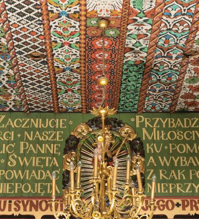 Zdjęcie nr 5: Polichromia pokrywa praktycznie całe wnętrze kościoła wraz z przedsionkiem. Przy wejściu, na stropie pod wieżą znajduje się polichromia patronowa. Jest wielobrawna, z motywami architektonicznymi, geometrycznymi, roślinno-kwiatowymi i figuralnymi – jeleniami, parami gołąbków, orłami, smokami. Wśród nich postać jeźdźca z kopią i grupa ludzi udających się na polowanie, poniżej których napis „Odbudowę kościoła, urządzenie wnętrza i rekonstrukcję dokonano staraniem Ks(iędza) Andrzeja Braszki / w czasie od lipca 1932 do grudnia r(oku) (19)39. / Pracę rozpoczął Władysław Cichoń + Skończył Adam Stalony-Dobrzański z Eugeniuszem Pisarkiem”. W polichromii przedsionka przeważają kolory  biały, czerwony, zielony, niebieski, żółty i czarny. Ponad wejściem do nawy napis  „ZACZNIJCIE / WARGI NASZE / CHWALIĆ PANNĘ / ŚWIĘTĄ / ZACZNIJCIE OPOWIADAĆ / CZEŚĆ JEJ NIEPOJĘTĄ”  i po drugieh stronie „PRZYBĄDŹ NAM. MIŁOŚCIWA PANI / KU POMOCY / A WYBAW NAS / Z RĄK POTĘŻNYCH / NIEPRZYJACIÓŁ MOCY”. Poniżej „CHWAŁA OJCU I SYNOWI JEGO PRZEDWIECZNEMU”.
W prezbiterium na ścianie i na suficie imitacja kasetonów z rozetami z przewagą koloru zielonego uzupełnionego czerwonym na ścianie i czarnym oraz bladożółtym na stropie. W centrum sufitu postać Matki Boskiej z Dzieciątkiem na lewym ramieniu, za którymi dwaj aniołowie skłaniający głowy. Maria ma poważną twarz o delikatnych rysach, ciemne oczy i wąski nos, na głowie otwartą koronę, wokół niej nimb. Jest ubrana w jasną sukienkę i intensywnie niebieski płaszcz. Dzieciątko prawą ręką błogosławi, lewą trzyma rękę Marii. Ma owalną, delikatną twarz, a na sobie jasną tunikę i zamkniętą koronę. 
W nawie, pośród takich samych kasetonów jak w prezbiterium, na sklepieniu wyobrażenie św. Michała Archanioła zabijającego szatana. Ponad nim postać anioła splatającego dłonie pod brodą. Archanioł spogląda pod stopy, w prawej ręce trzyma skierowany ostrzem w stronę potwora miecz, lewą ma opuszczoną do boku. Ma na sobie zieloną tunikę przewiązaną szerokim, góralskim pasem i czerwony płaszcz. Jasne postrzępione plamy ponad jego plecami sugerują skrzydła. Anioł powyżej jest ubrany w czerwoną sukienkę, nad nim płynnie uchodzą w górę ulistnione linie. Na ścianach nawy, pod linią stropu, rząd klęczących aniołów między kwitnącymi kwiatami. Każdy jest ubrany w zielonożółtą sukienkę i sandały, ma włosy do ramion i złoty nimb. Skrzydła z różnie ułożonych piór są wielobarwne. Anioły klęczą na linii ornamentu, ściana poniżej jest jasnoniebieska, z napisem powyżej opisanych przedstawień. 
Na skośnych fragmentach stropu imitacja drobniejszych kasetonów o falistym zarysie, wypełnionych krzyżami równoramiennymi. Wszystkie ciemnożółte, większość na czarnym tle, niektóre na tle zielonym tworzą kształt rombów. Na krawędzi motywy geometryczne, które mogą sugerować płonące serca. 
Na parapecie chóru fragmenty dawnej polichromii o motywach liściasto-wiciowych z rozwiniętymi kwiatami i motywem żołędzia. Między nimi ludzka głowa. Malowidło utrzymane w dominującym kolorze brązu, z elementami zielonymi i czerwonymi. 
