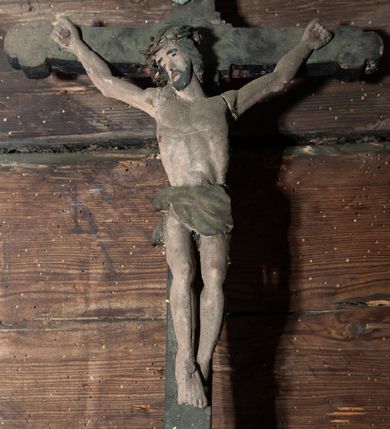Zdjęcie nr 1: Wizerunek Chrystusa przybitego trzema gwoździami do krzyża łacińskiego. Ciało wyprostowane, ręce rozciągnięte do boku, barki uniesione, nogi delikatnie ugięte w kolanach. Głowa opada na prawy bok. Jezus ma podłużną twarz, usta i oczy zamknięte, nos prosty; okala ją czarna broda oraz zwijające się w fale włosy opadające na plecy. Na głowie ciemnobrązowa korona cierniowa. Biodra otacza złote (?), marszczone  w grube fałdy perizonium z węzłem na prawym boku.  W miejscach przebić gwoździami oraz w  ranie w boku ślady krwi. Krzyż gładki, o ramionach zakończonych trójlistnie, na górnej belce titulus w formie zwoju z literami „IN/RI”. Polichromia w partiach ciała naturalistyczna, krzyż czarny. 