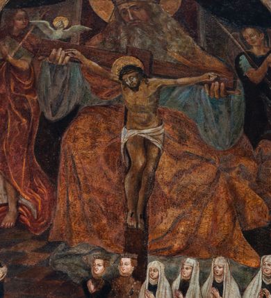 Zdjęcie nr 3: Obraz w formie stojącego prostokąta z wyodrębnionym w górnej części łukiem półkolistym, w którego przyłuczach znajduje się ryta w zaprawie i złocona wić roślinna. W centrum przedstawienia tronujący Bóg Ojciec, który obiema rękami trzyma ramiona krzyża, do którego przybity jest Chrystus. Na krawędzi poziomej belki siedzi gołębica Ducha Świętego. Bóg ukazany frontalnie, z głową przechyloną na prawe ramię. Twarz ma pociągłą, o starczych rysach, okrągłych oczach, dużym nosie i pełnych ustach; okoloną długą, siwą brodą i włosami opadającymi na ramiona. Na głowie ma tiarę, a wokół niej nimb zamknięty. Ubrany jest w jasnoniebieską, luźną tunikę oraz jasnobrązowy płaszcz zarzucony na ramiona i nogi. Chrystus o znacznie mniejszych rozmiarach, przybity jest do krzyża czterema gwoździami. Jego ciało jest w lekkim zwisie, o szeroko rozłożonych ramionach, głowa opada na prawy bark. Twarz ma pociągłą, o zamkniętych oczach, okoloną krótką brodą i włosami sięgającymi ramion. Na głowie ma koronę cierniową, a wokół niej nimb zamknięty. Ciało ma szczupłe i muskularne. Przez biodra przewiązane krótkie, białe perizonium. Postać Boga Ojca flankują dwa anioły zwrócone na zewnątrz, z głowami skierowanymi do środka oraz rękami złożonymi w geście modlitwy. Anioł po jego prawej stronie trzyma berło, ubrany jest w jasną tunikę i czerwony płaszcz. Anioł po jego lewej trzyma włócznię i ubrany jest w niebieską tunikę. W tle widoczne oparcie tronu. Scena ujęta u góry podwiązaną po bokach ciemną draperią. W dolnej części obrazu na szachownicowej posadzce ukazana niewielkich rozmiarów rodzina fundatorki obrazu. W prawej dolnej części obrazu przedstawiono sześć klęczących kobiet, zwróconych w swoją prawą stronę, z dłońmi złożonymi w geście modlitwy, jedna z nich z opuszczonymi, skrzyżowanymi dłońmi. Cztery spośród nich to mężatki ubrane w czarne suknie, białe rańtuchy z podwikami, przed ostatnią znajduje się tarcza z godłem herbu Leliwa. Dwie pozostałe ukazane w strojach niezamężnych panien, w bogato zdobionych sukniach z szerokimi rękawami i kryzami, z toczenicami na głowach. Przed kobietami klęczy trójka dzieci z dłońmi złożonymi w geście modlitwy. Dzieci ukazane w różnym wieku, ubrane są w białe suknie z kryzami wokół szyi. W lewej części obrazu klęczy zwrócony w swoją lewą stronę mężczyzna, z dłońmi złożonymi w geście modlitwy ubrany w czarną szubę. Przed nim tarcza z godłem herbu Trąby.



