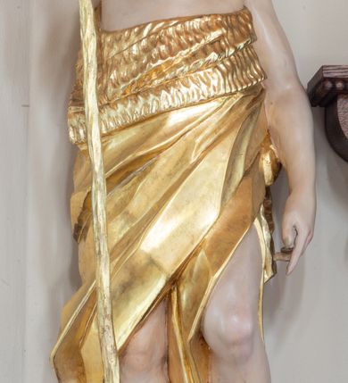 Zdjęcie nr 3: Święty ukazany frontalnie, z głową skierowaną w lewo, w prawej ręce trzyma laskę zakończoną krzyżem, lewą ma opuszczoną wzdłuż boku, lewą nogę opiera na rzeźbionym kamieniu, na którym stoi baranek. Twarz ma pociągłą, o migdałowatych oczach skierowanych w górę, prostym nosie i rozchylonych ustach, okoloną krótką, kręconą brodą oraz kręconymi włosami opadającymi na ramiona. Ubrany jest w melotę opasującą jego korpus i nogi, odsłaniającą część klatki piersiowej i ramiona oraz lewą nogę. Polichromia ciała naturalistyczna, włosy i broda brązowe, strój i laska złocone, baranek srebrzony. 