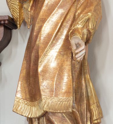 Zdjęcie nr 3: Święty zwrócony w trzech czwartych w prawo, lekko odchylony, prawą rękę kładzie na piersi, lewą wyciąga w bok,  lewa noga oparta na stosie kamieni. Twarz o młodzieńczych rysach, owalna, o migdałowatych oczach skierowanych w górę, prostym nosie i pełnych, rozchylonych ustach, okolona krótkimi i kręconymi włosami. Ubrany jest w albę oraz dalmatykę z frędzlą przy brzegach. Polichromia ciała naturalistyczna, włosy brązowe, strój złocony. 