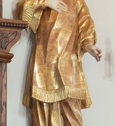 Zdjęcie nr 2: Święty zwrócony w trzech czwartych w prawo, lekko odchylony, prawą rękę kładzie na piersi, lewą wyciąga w bok,  lewa noga oparta na stosie kamieni. Twarz o młodzieńczych rysach, owalna, o migdałowatych oczach skierowanych w górę, prostym nosie i pełnych, rozchylonych ustach, okolona krótkimi i kręconymi włosami. Ubrany jest w albę oraz dalmatykę z frędzlą przy brzegach. Polichromia ciała naturalistyczna, włosy brązowe, strój złocony. 