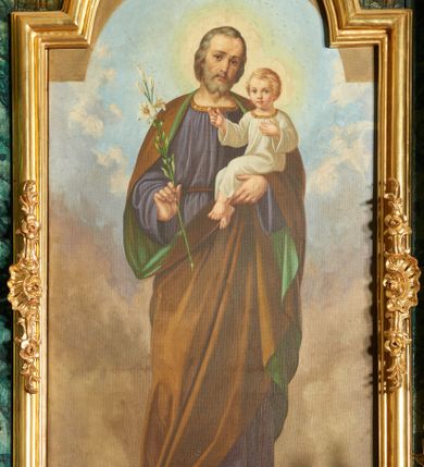 Zdjęcie nr 1: Podobrazie w formie stojącego prostokąta, pole obrazowe zamknięta łukiem półkolistym nadwieszonym. W centrum św. Józef ukazany w całej postaci, frontalnie, w wykroku, z głową przechyloną na lewe ramię. W prawej, ugiętej ręce trzyma gałązkę lilii, lewą podtrzymuje Dzieciątko. Twarz ma pociągłą, o delikatnych rysach, dużych oczach, prostym nosie i pełnych ustach, okoloną krótkimi, siwymi włosami i brodą. Ubrany jest w obszerną, fioletową tunikę, przepasaną w talii, ze złoconą lamówką wokół otworu na szyję. Na ramiona ma narzucony brązowy płaszcz z zieloną podszewką, który podtrzymuje z przodu lewą dłonią. Na stopach ma sandały. Dzieciątko ukazane w pozycji siedzącej, zwrócone w trzech czwartych w lewo, z głową przedstawioną frontalnie. Twarz ma okrągłą, o dużych oczach, małym nosie i pełnych ustach, okoloną krótkimi, jasnymi włosami. Ubrane jest w białą, luźną tunikę ze złoconą lamówką wokół otworu na szyję. Postacie ukazane na tle nieba wypełnionego błekitno-szarymi obłokami.


