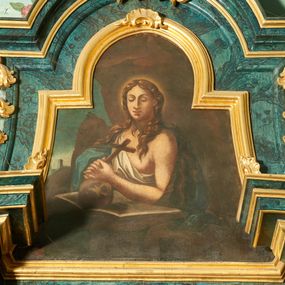 Zdjęcie nr 1: Obraz w formie trapezu zamkniętego łukiem półkolistym nadwieszonym, o wklęsłych bokach. W centrum ukazana półpostać św. Marii Magdaleny w jaskini. Święta zwrócona w trzech czwartych w prawo, ze splecionymi dłońmi trzymającymi krzyż, opartymi na czaszce leżącej na otwartej księdze. Twarz ma owalną, o dużych, okrągłych oczach skierowany w dół, wąskim, długim nosie i pełnych ustach. Włosy ma długie, falowane, opadające na ramiona i plecy. Ubrana jest w białą szatę przewiązaną diagonalnie przez prawe ramię, odsłaniającą pierś oraz niebieski płaszcz zarzucony na plecy i prawe ramię. Święta ukazana na tle groty, z widocznym po lewej stronie górzystym pejzażem z wieżą. 




