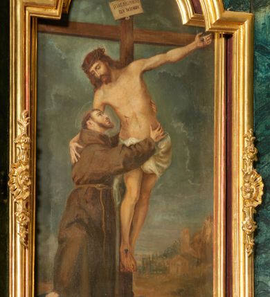 Zdjęcie nr 1: Obraz w formie stojącego prostokąta zamkniętego łukiem półkolistym nadwieszonym, przedstawiający św. Franciszka obejmującego Chrystusa na krzyżu. Jezus przybity do krzyża znajdującego się w centrum kompozycji. Ukazany frontalnie, przechylony w prawą stronę, jedną ręką obejmuje św. Franciszka, nogi ma lekko ugięte w kolanach, stopy skrzyżowane w układzie prawa na lewą. Twarz ma pociągłą, z oczami skierowanymi w dół, prostym nosem; okoloną krótką brodą oraz włosami sięgającymi ramion. Na głowie ma koronę cierniową. Ciało szczupłe i umięśnione, z krwawiącymi ranami. Biodra przewiązane krótkim, białym perizonium. Święty Franciszek ukazany w pozycji stojącej, z profilu, z uniesioną głową, prawą nogę wspiera na niebieskiej kuli, obiema rękami obejmuje ciało Chrystusa. Twarz ma szczupłą, z oczami skierowanymi w górę, prostym nosem i pełnymi ustami, okoloną ciemnym zarostem i krótkimi włosami, na głowie tonsura. Ubrany jest w brązowy habit z kapturem, przepasany sznurem. Na dłoniach ma stygmaty. Scena ukazana na tle pejzażu, z widoczną w oddali panoramą miasta. Niebo szaro-niebieskie, zachmurzone. Obraz ujęty drewnianą, złoconą, profilowaną ramą.