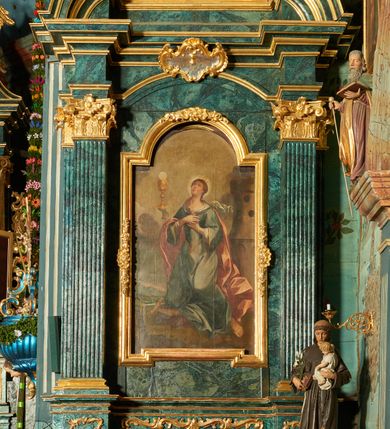 Zdjęcie nr 2: Obraz w formie stojącego prostokąta zamkniętego łukiem półkolistym nadwieszonym, przedstawiający św. Franciszka obejmującego Chrystusa na krzyżu. Jezus przybity do krzyża znajdującego się w centrum kompozycji. Ukazany frontalnie, przechylony w prawą stronę, jedną ręką obejmuje św. Franciszka, nogi ma lekko ugięte w kolanach, stopy skrzyżowane w układzie prawa na lewą. Twarz ma pociągłą, z oczami skierowanymi w dół, prostym nosem; okoloną krótką brodą oraz włosami sięgającymi ramion. Na głowie ma koronę cierniową. Ciało szczupłe i umięśnione, z krwawiącymi ranami. Biodra przewiązane krótkim, białym perizonium. Święty Franciszek ukazany w pozycji stojącej, z profilu, z uniesioną głową, prawą nogę wspiera na niebieskiej kuli, obiema rękami obejmuje ciało Chrystusa. Twarz ma szczupłą, z oczami skierowanymi w górę, prostym nosem i pełnymi ustami, okoloną ciemnym zarostem i krótkimi włosami, na głowie tonsura. Ubrany jest w brązowy habit z kapturem, przepasany sznurem. Na dłoniach ma stygmaty. Scena ukazana na tle pejzażu, z widoczną w oddali panoramą miasta. Niebo szaro-niebieskie, zachmurzone. Obraz ujęty drewnianą, złoconą, profilowaną ramą.