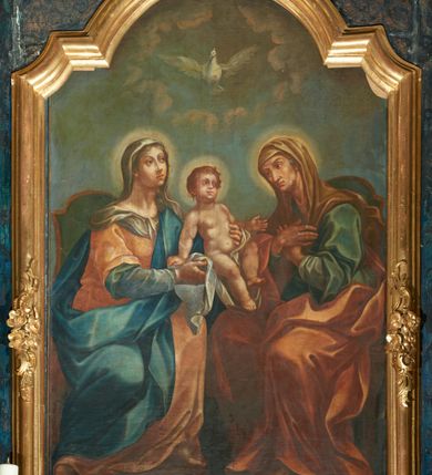 Zdjęcie nr 1: Obraz w formie stojącego prostokąta zamkniętego łukiem półkolistym nadwieszonym z uskokiem. W centrum ukazane Maria i św. Anna, siedzące na fotelach, pomiędzy którymi podtrzymywane jest Dzieciątko Jezus. Maria w lewej części obrazu, zwrócona w trzech czwartych w lewo, obiema rękami podtrzymuje przed sobą Dzieciątko, lewą nogę opiera na podnóżku. Twarz ma owalną, o małych, okrągłych oczach, uniesionych, łukowatych brwiach, wąskim, długim nosie i małych ustach, okoloną jasnymi włosami ukrytymi pod welonem. Ubrana jest w niebieską suknię spodnią z długimi rękawami, jasnopomarańczową suknię wierzchnią z krótkimi, szerokimi rękawami oraz w niebieski płaszcz przepasany diagonalnie przez lewe ramie i opadający na prawą nogę. Na głowie ma szary welon, opadający na ramię, na stopach złote sandały. Dzieciątko ukazane w pozycji siedzącej, zwrócone w trzech czwartych w lewo, oparte na prawej ręce, lewą wyciąga ku św. Annie. Twarz ma okrągłą, o pełnych policzkach, małych, okrągłych oczach, uniesionych brwiach i pełnych ustach. Ciało ma pulchne, przesłonięte w partii podbrzusza białą pieluszką. W prawej części obrazu ukazana św. Anna, zwrócona w trzech czwartych w prawo, z pochyloną głową i rękami skrzyżowanymi na piersi. Twarz ma owalną, wychudzoną, o małych okrągłych oczach, uniesionych brwiach, lekko garbatym nosie i małych ustach. Ubrana jest w jasnoniebieską suknię spodnią z długimi rękawami, niebieską suknię wierzchnią z krótkimi, szerokimi rękawami oraz w pomarańczowy płaszcz zarzucony na prawe ramię i opadający na kolana. Na głowie ma jasnobrązowy welon, opadający na ramiona i plecy, na stopach złote sandały. Wokół głów postaci nimby. Nad nimi unosi się gołębica Ducha Świętego w otoku z obłoków. W tle widoczne szaro-niebieskie niebo. 
