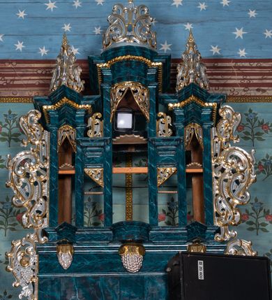Zdjęcie nr 3: Szafa architektoniczna, pięcioosiowa, na profilowanym cokole, podtrzymywanym przez trzy wsporniki zakończone szyszkami. Oś środkowa najwyższa, dwie skrajne niższe, ujęte pilastrami podtrzymującymi fragmenty belkowania wyłamanego półkoliście i pod kątem, z prześwitami na piszczałki w formie stojącego prostokąta. Dwie środkowe osie najniższe, zakończone fragmentami niepełnego belkowania, z prześwitami na piszczałki w formie stojącego prostokąta. Oś środkowa i dwie skrajne zwieńczone ornamentalnymi małżowinowo-chrząstkowymi szczytami. Na belkowaniu osi środkowych fragmenty ornamentu małżowinowo-chrząstkowego, którym zdobi również prześwity na piszczałki w górnej części. Szafa i jej cokół flankowane rozłożystymi uszami utworzonymi z ornamentu małżowinowo-chrząstkowego z motywami owoców i winnego grona. Struktura polichromowana na sposób imitujący marmoryzację w kolorze niebieskim, ornamentyka złocona i srebrzona.