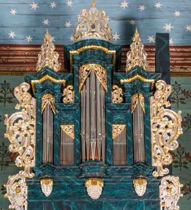 Zdjęcie nr 1: Szafa architektoniczna, pięcioosiowa, na profilowanym cokole, podtrzymywanym przez trzy wsporniki zakończone szyszkami. Oś środkowa najwyższa, dwie skrajne niższe, ujęte pilastrami podtrzymującymi fragmenty belkowania wyłamanego półkoliście i pod kątem, z prześwitami na piszczałki w formie stojącego prostokąta. Dwie środkowe osie najniższe, zakończone fragmentami niepełnego belkowania, z prześwitami na piszczałki w formie stojącego prostokąta. Oś środkowa i dwie skrajne zwieńczone ornamentalnymi małżowinowo-chrząstkowymi szczytami. Na belkowaniu osi środkowych fragmenty ornamentu małżowinowo-chrząstkowego, którym zdobi również prześwity na piszczałki w górnej części. Szafa i jej cokół flankowane rozłożystymi uszami utworzonymi z ornamentu małżowinowo-chrząstkowego z motywami owoców i winnego grona. Struktura polichromowana na sposób imitujący marmoryzację w kolorze niebieskim, ornamentyka złocona i srebrzona.