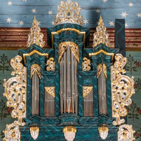 Zdjęcie nr 1: Szafa architektoniczna, pięcioosiowa, na profilowanym cokole, podtrzymywanym przez trzy wsporniki zakończone szyszkami. Oś środkowa najwyższa, dwie skrajne niższe, ujęte pilastrami podtrzymującymi fragmenty belkowania wyłamanego półkoliście i pod kątem, z prześwitami na piszczałki w formie stojącego prostokąta. Dwie środkowe osie najniższe, zakończone fragmentami niepełnego belkowania, z prześwitami na piszczałki w formie stojącego prostokąta. Oś środkowa i dwie skrajne zwieńczone ornamentalnymi małżowinowo-chrząstkowymi szczytami. Na belkowaniu osi środkowych fragmenty ornamentu małżowinowo-chrząstkowego, którym zdobi również prześwity na piszczałki w górnej części. Szafa i jej cokół flankowane rozłożystymi uszami utworzonymi z ornamentu małżowinowo-chrząstkowego z motywami owoców i winnego grona. Struktura polichromowana na sposób imitujący marmoryzację w kolorze niebieskim, ornamentyka złocona i srebrzona.