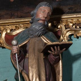 Zdjęcie nr 1: Figura ścięta z tyłu, ustawiona na niskiej podstawie. Święty ukazany frontalnie, z głową przechyloną na lewe ramię, o delikatnie esowato wygiętej sylwetce. Obie ręce ma wyciągnięte przed siebie, lewą podtrzymuje otwartą księgę, w prawej trzyma laskę zakończoną kulą. Twarz ma pociągłą, o wąskich oczach i nosie oraz rozchylonych ustach, okoloną długą, szarą brodą rozwianą w bok oraz krótkimi, siwymi włosami. Ubrany jest w brązową tunikę przepasaną w talii, ze złoconym szkaplerzem oraz zielony płaszcz ze złoconą podszewką, zarzucony na ramiona i zapięty pod szyją. Polichromia ciała naturalistyczna.

