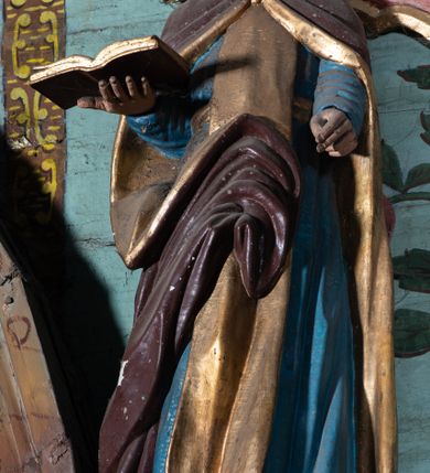 Zdjęcie nr 2: Figura ścięta z tyłu, ustawiona na niskiej podstawie. Święty ukazany frontalnie, z głową przechyloną na prawe ramię, obie ręce wyciąga do przodu, prawą podtrzymuje otwartą księgę. Twarz ma pociągłą, o wąskich oczach i nosie oraz otwartych ustach, okoloną gęstą brodą oraz włosami sięgającymi ramion, na głowie ma łysinę. Ubrany jest w niebieską suknię, przepasaną w talii, ze złoconym szkaplerzem oraz brązowy płaszcz o złoconej podszewce, zarzucony na ramiona, zapięty pod szyją i zawinięty z przodu postaci. Polichromia ciała naturalistyczna. 

