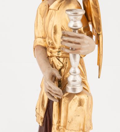 Zdjęcie nr 2: Pełnoplastyczne figury klęczących na jedno kolano aniołów, ustawionych na niskich podstawach. Postacie ukazane są z profilu, z głowami skierowanymi frontalnie. Na ugiętych kolanach trzymają srebrzone lichtarze, przytrzymując je obiema rękami, z boku i od spodu. Twarze mają podłużne, trójkątne, o dużych, migdałowatych, opadających oczach, prostych nosach i wąskich ustach, okolone silnie kręconymi włosami, układającymi się po bokach głowy, a nad czołem tworzące czub. Ubrane są w długie ciemnoczerwone suknie spodnie i złocone suknie wierzchnie z kołnierzykami, sięgające kolan, z podwiniętymi rękawami, przepasane w talii szarfami. Skrzydła mają małe, złocone, złożone po bokach postaci. Polichromia ciała naturalistyczna. 



