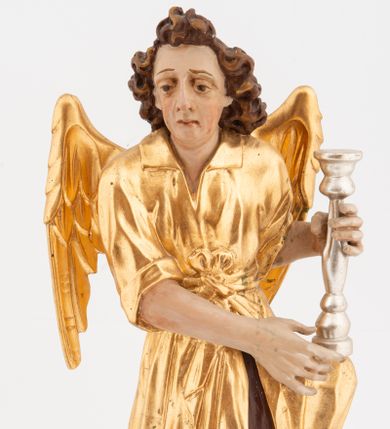 Zdjęcie nr 1: Pełnoplastyczne figury klęczących na jedno kolano aniołów, ustawionych na niskich podstawach. Postacie ukazane są z profilu, z głowami skierowanymi frontalnie. Na ugiętych kolanach trzymają srebrzone lichtarze, przytrzymując je obiema rękami, z boku i od spodu. Twarze mają podłużne, trójkątne, o dużych, migdałowatych, opadających oczach, prostych nosach i wąskich ustach, okolone silnie kręconymi włosami, układającymi się po bokach głowy, a nad czołem tworzące czub. Ubrane są w długie ciemnoczerwone suknie spodnie i złocone suknie wierzchnie z kołnierzykami, sięgające kolan, z podwiniętymi rękawami, przepasane w talii szarfami. Skrzydła mają małe, złocone, złożone po bokach postaci. Polichromia ciała naturalistyczna. 



