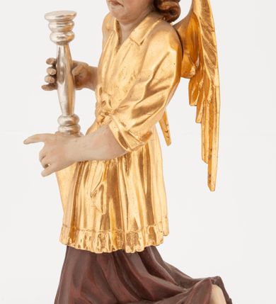 Zdjęcie nr 7: Pełnoplastyczne figury klęczących na jedno kolano aniołów, ustawionych na niskich podstawach. Postacie ukazane są z profilu, z głowami skierowanymi frontalnie. Na ugiętych kolanach trzymają srebrzone lichtarze, przytrzymując je obiema rękami, z boku i od spodu. Twarze mają podłużne, trójkątne, o dużych, migdałowatych, opadających oczach, prostych nosach i wąskich ustach, okolone silnie kręconymi włosami, układającymi się po bokach głowy, a nad czołem tworzące czub. Ubrane są w długie ciemnoczerwone suknie spodnie i złocone suknie wierzchnie z kołnierzykami, sięgające kolan, z podwiniętymi rękawami, przepasane w talii szarfami. Skrzydła mają małe, złocone, złożone po bokach postaci. Polichromia ciała naturalistyczna. 



