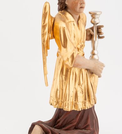 Zdjęcie nr 3: Pełnoplastyczne figury klęczących na jedno kolano aniołów, ustawionych na niskich podstawach. Postacie ukazane są z profilu, z głowami skierowanymi frontalnie. Na ugiętych kolanach trzymają srebrzone lichtarze, przytrzymując je obiema rękami, z boku i od spodu. Twarze mają podłużne, trójkątne, o dużych, migdałowatych, opadających oczach, prostych nosach i wąskich ustach, okolone silnie kręconymi włosami, układającymi się po bokach głowy, a nad czołem tworzące czub. Ubrane są w długie ciemnoczerwone suknie spodnie i złocone suknie wierzchnie z kołnierzykami, sięgające kolan, z podwiniętymi rękawami, przepasane w talii szarfami. Skrzydła mają małe, złocone, złożone po bokach postaci. Polichromia ciała naturalistyczna. 



