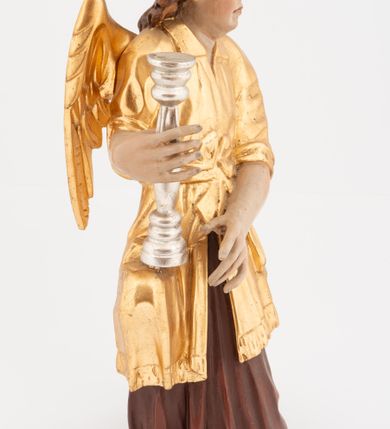 Zdjęcie nr 5: Pełnoplastyczne figury klęczących na jedno kolano aniołów, ustawionych na niskich podstawach. Postacie ukazane są z profilu, z głowami skierowanymi frontalnie. Na ugiętych kolanach trzymają srebrzone lichtarze, przytrzymując je obiema rękami, z boku i od spodu. Twarze mają podłużne, trójkątne, o dużych, migdałowatych, opadających oczach, prostych nosach i wąskich ustach, okolone silnie kręconymi włosami, układającymi się po bokach głowy, a nad czołem tworzące czub. Ubrane są w długie ciemnoczerwone suknie spodnie i złocone suknie wierzchnie z kołnierzykami, sięgające kolan, z podwiniętymi rękawami, przepasane w talii szarfami. Skrzydła mają małe, złocone, złożone po bokach postaci. Polichromia ciała naturalistyczna. 



