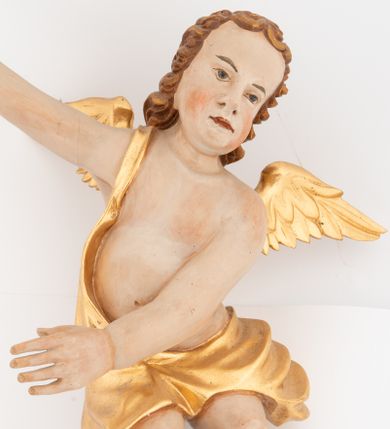 Zdjęcie nr 1: Dwie pełnoplastyczne rzeźby siedzących aniołów, ukazanych frontalnie, przechylonych w bok, z obiema rękami wyciągniętymi w przeciwną stronę. Twarze mają wydłużone, o pełnych policzkach, migdałowatych, dużych oczach, krótkich nosach i wąskich ustach, okolone krótkimi, kręconymi włosami. W partii bioder przewiązane złoconą tkaniną, zawiniętą na jednym ramieniu. Ciała mają pulchne, o nieproporcjonalnych względem korpusu kończynach. Ich skrzydła są złocone, małe i rozłożone na boki. Polichromia ciała naturalistyczna.