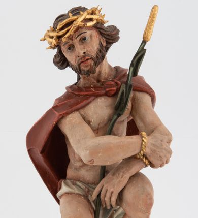 Zdjęcie nr 1: Rzeźba pełnoplastyczna, na podstawie w formie pnia. Chrystus ukazany w pozycji siedzącej, frontalnie, przechylony w prawo, z wysuniętą w bok prawą nogą. Ręce ma ugięte i lekko uniesione, skrzyżowane w nadgarstkach i przewiązane powrozem. Rękami obejmuje trzcinę. Twarz ma trójkątną, o migdałowatych oczach, dużym nosie i pełnych ustach; okoloną krótką brodą oraz silnie skręconymi po bokach głowy włosami, opadającymi na kark. Na głowie ma złoconą koronę cierniową. W partii bioder przewiązany jest białą tkaniną. Na ramiona ma narzucony czerwony płaszcz zawiązany pod szyją. Jego ciało jest szczupłe, ale muskularne. Polichromia ciała naturalistyczna z zaznaczonymi śladami męki. 

