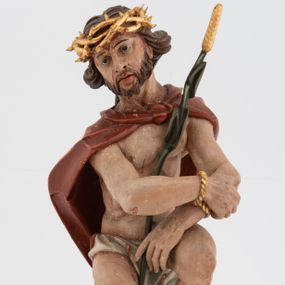 Zdjęcie nr 1: Rzeźba pełnoplastyczna, na podstawie w formie pnia. Chrystus ukazany w pozycji siedzącej, frontalnie, przechylony w prawo, z wysuniętą w bok prawą nogą. Ręce ma ugięte i lekko uniesione, skrzyżowane w nadgarstkach i przewiązane powrozem. Rękami obejmuje trzcinę. Twarz ma trójkątną, o migdałowatych oczach, dużym nosie i pełnych ustach; okoloną krótką brodą oraz silnie skręconymi po bokach głowy włosami, opadającymi na kark. Na głowie ma złoconą koronę cierniową. W partii bioder przewiązany jest białą tkaniną. Na ramiona ma narzucony czerwony płaszcz zawiązany pod szyją. Jego ciało jest szczupłe, ale muskularne. Polichromia ciała naturalistyczna z zaznaczonymi śladami męki. 

