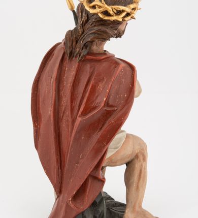 Zdjęcie nr 7: Rzeźba pełnoplastyczna, na podstawie w formie pnia. Chrystus ukazany w pozycji siedzącej, frontalnie, przechylony w prawo, z wysuniętą w bok prawą nogą. Ręce ma ugięte i lekko uniesione, skrzyżowane w nadgarstkach i przewiązane powrozem. Rękami obejmuje trzcinę. Twarz ma trójkątną, o migdałowatych oczach, dużym nosie i pełnych ustach; okoloną krótką brodą oraz silnie skręconymi po bokach głowy włosami, opadającymi na kark. Na głowie ma złoconą koronę cierniową. W partii bioder przewiązany jest białą tkaniną. Na ramiona ma narzucony czerwony płaszcz zawiązany pod szyją. Jego ciało jest szczupłe, ale muskularne. Polichromia ciała naturalistyczna z zaznaczonymi śladami męki. 

