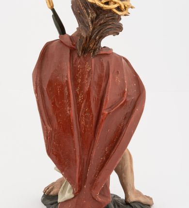 Zdjęcie nr 6: Rzeźba pełnoplastyczna, na podstawie w formie pnia. Chrystus ukazany w pozycji siedzącej, frontalnie, przechylony w prawo, z wysuniętą w bok prawą nogą. Ręce ma ugięte i lekko uniesione, skrzyżowane w nadgarstkach i przewiązane powrozem. Rękami obejmuje trzcinę. Twarz ma trójkątną, o migdałowatych oczach, dużym nosie i pełnych ustach; okoloną krótką brodą oraz silnie skręconymi po bokach głowy włosami, opadającymi na kark. Na głowie ma złoconą koronę cierniową. W partii bioder przewiązany jest białą tkaniną. Na ramiona ma narzucony czerwony płaszcz zawiązany pod szyją. Jego ciało jest szczupłe, ale muskularne. Polichromia ciała naturalistyczna z zaznaczonymi śladami męki. 

